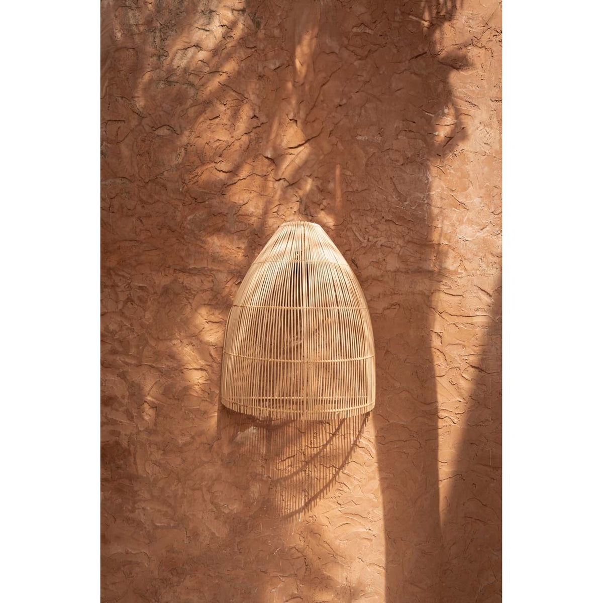 Abat-jour Lalo en rotin naturel fixé sur un mur en terre avec son ombre tressée