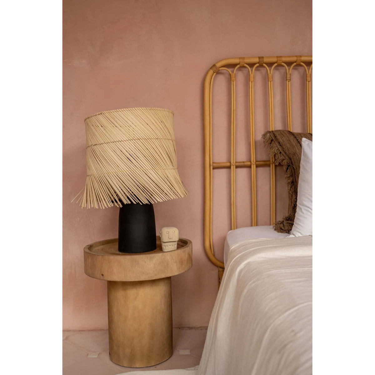 Abat-jour en rotin naturel sur un pied de lampe noir non fourni posé sur une table de chevet en bois