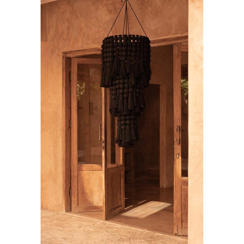 Lustre Nomad en coton noir suspendu devant une porte vitrée en bois dans un mur en enduit couleur terre