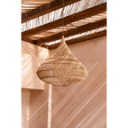 Abat-jour Drop en rotin suspendu sous une pergola devant un mur rose ocre
