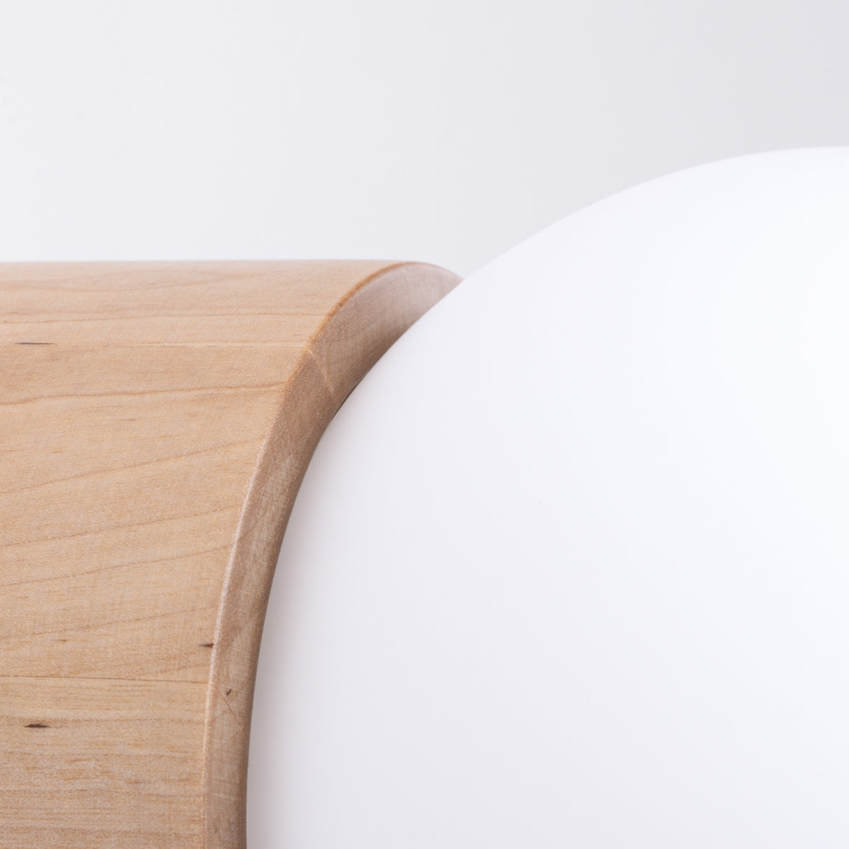Détail du cylindre en bois naturel veiné de l'applique Boomo contre sa boule en verre opale