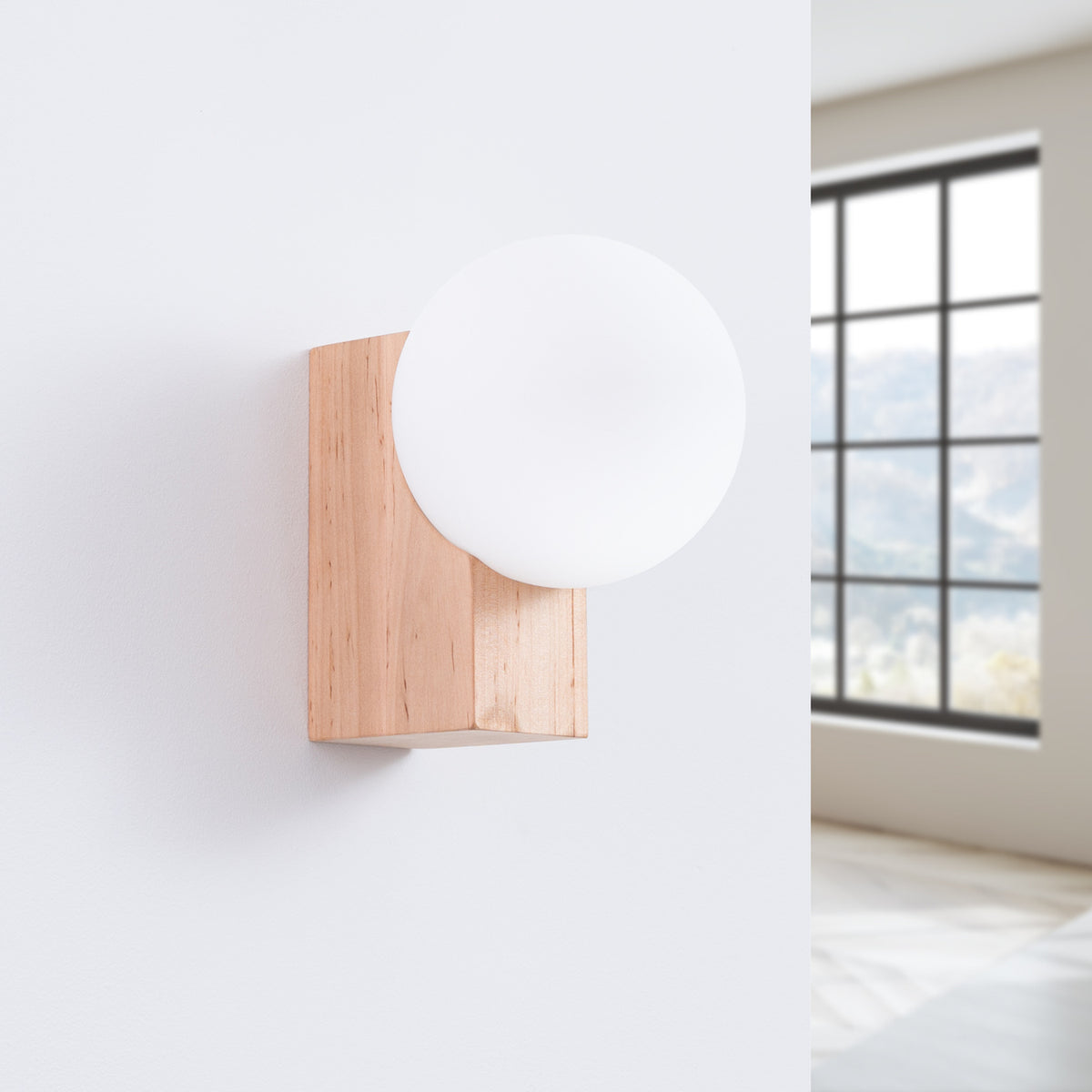 Applique Bulbo bois naturel et globe opale fixée sur un mur blanc près d'une fenêtre