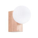 Applique murale Bulbo globe en verre opale blanc posé contre un bloc de bois naturel sur fond blanc