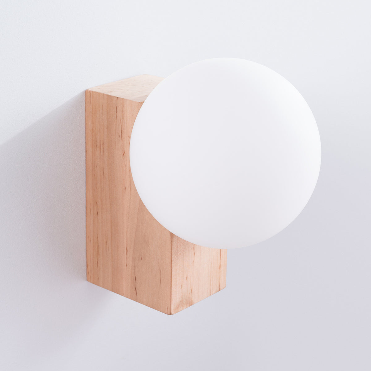 Applique Bulbo vue de trois quarts avec son globe opale qui déborde du bloc de bois