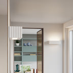 Applique Rigata en céramique blanche allumée près d'une porte vitrée avec un luminaire carré cannelé au premier plan