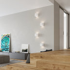Quatre appliques Leo céramique blanche allumées sur le mur d'un séjour au parquet en bois clair