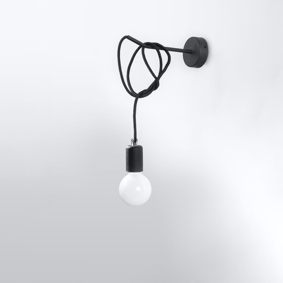 Applique Edison noire fixée sur un mur clair avec son câble textile enroulé autour du bras et son ampoule globe pendante