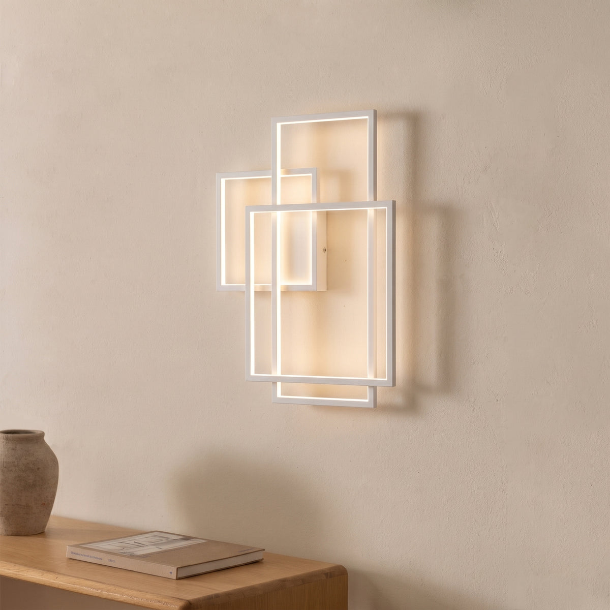Applique Geometric métal blanc allumée au-dessus d'une console en bois avec un vase en terre et un livre