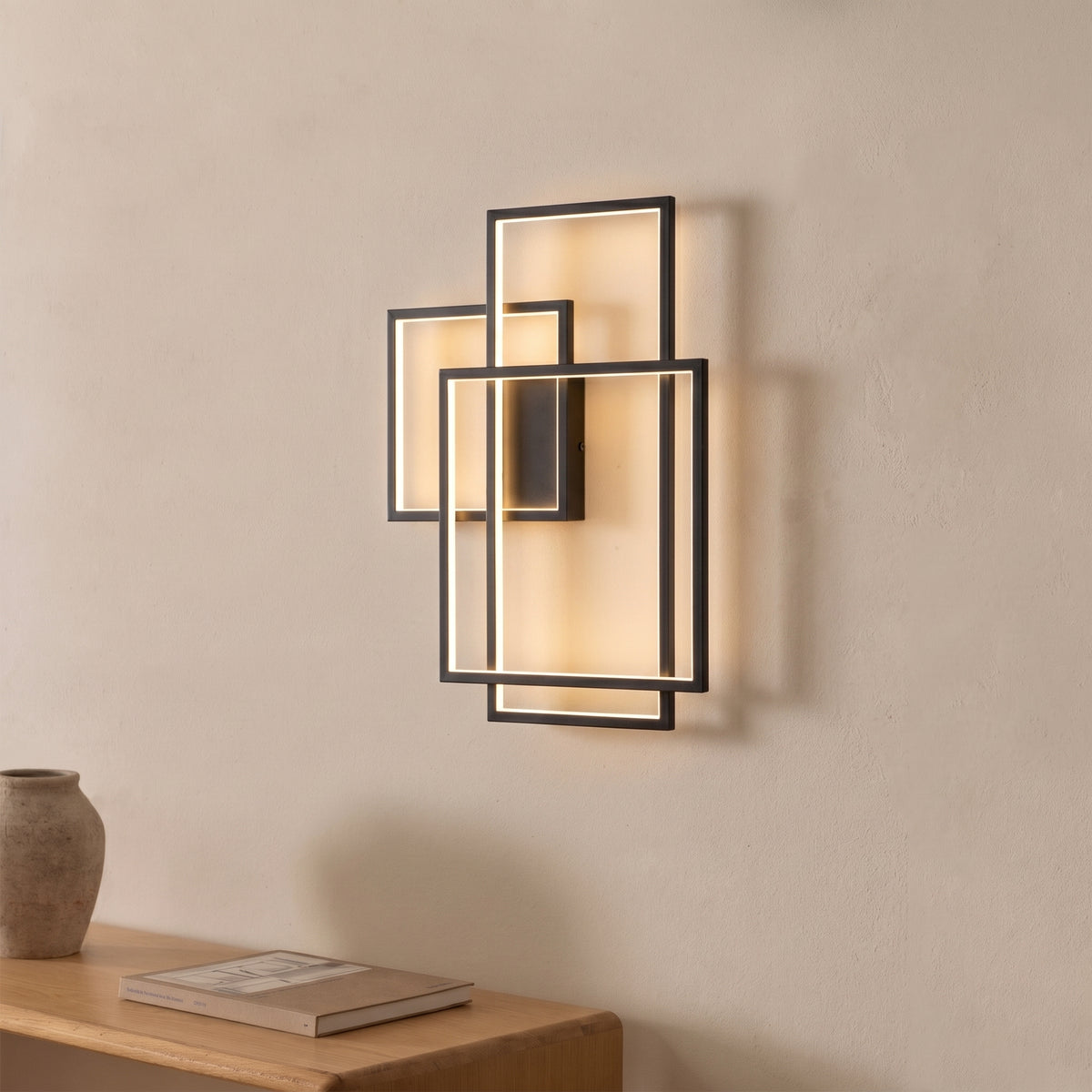 Applique Geometric métal noir allumée au-dessus d'une console en bois avec un vase en terre et un livre