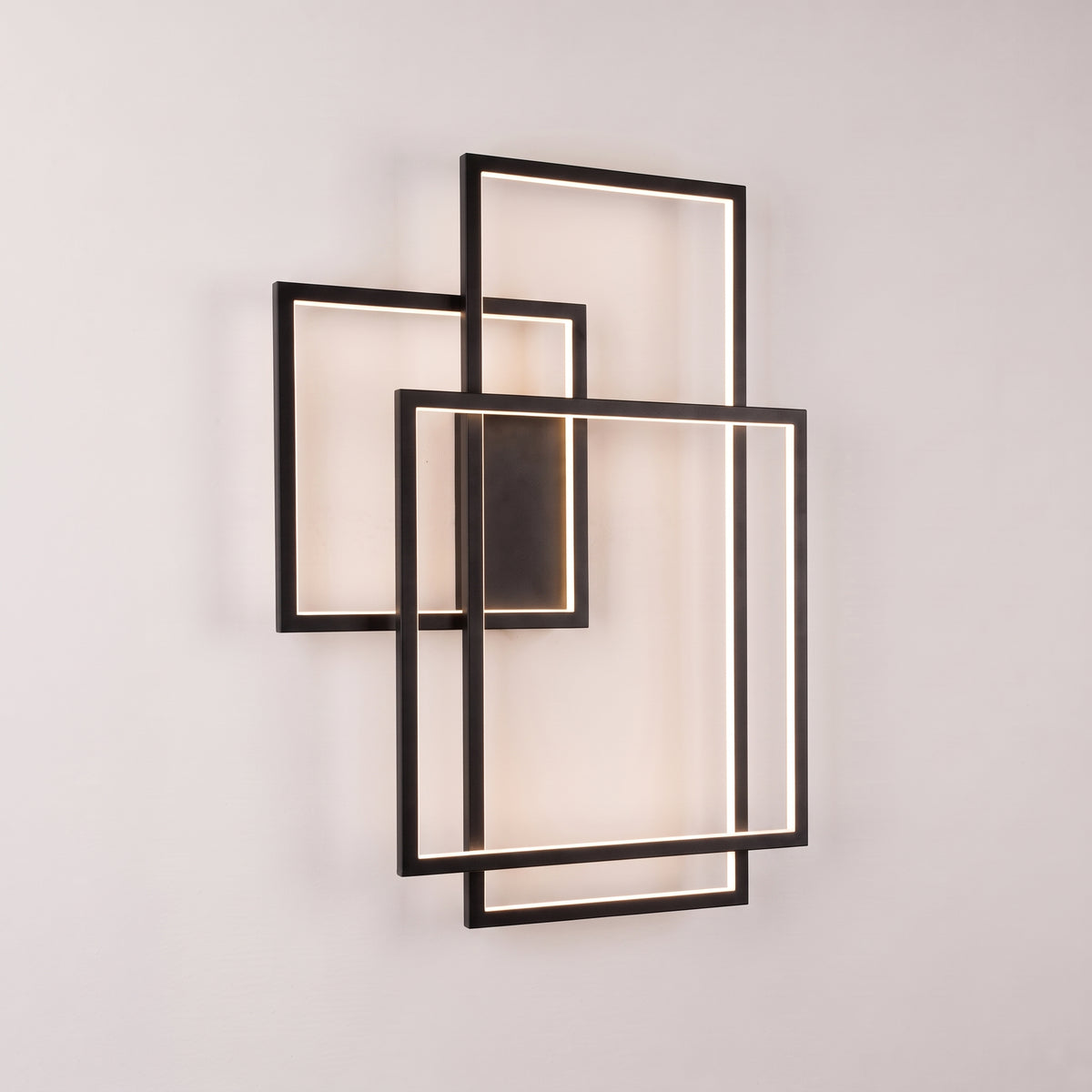 Applique murale Geometric LED en métal noir allumée, trois cadres rectangulaires superposés posés à la verticale sur un mur clair