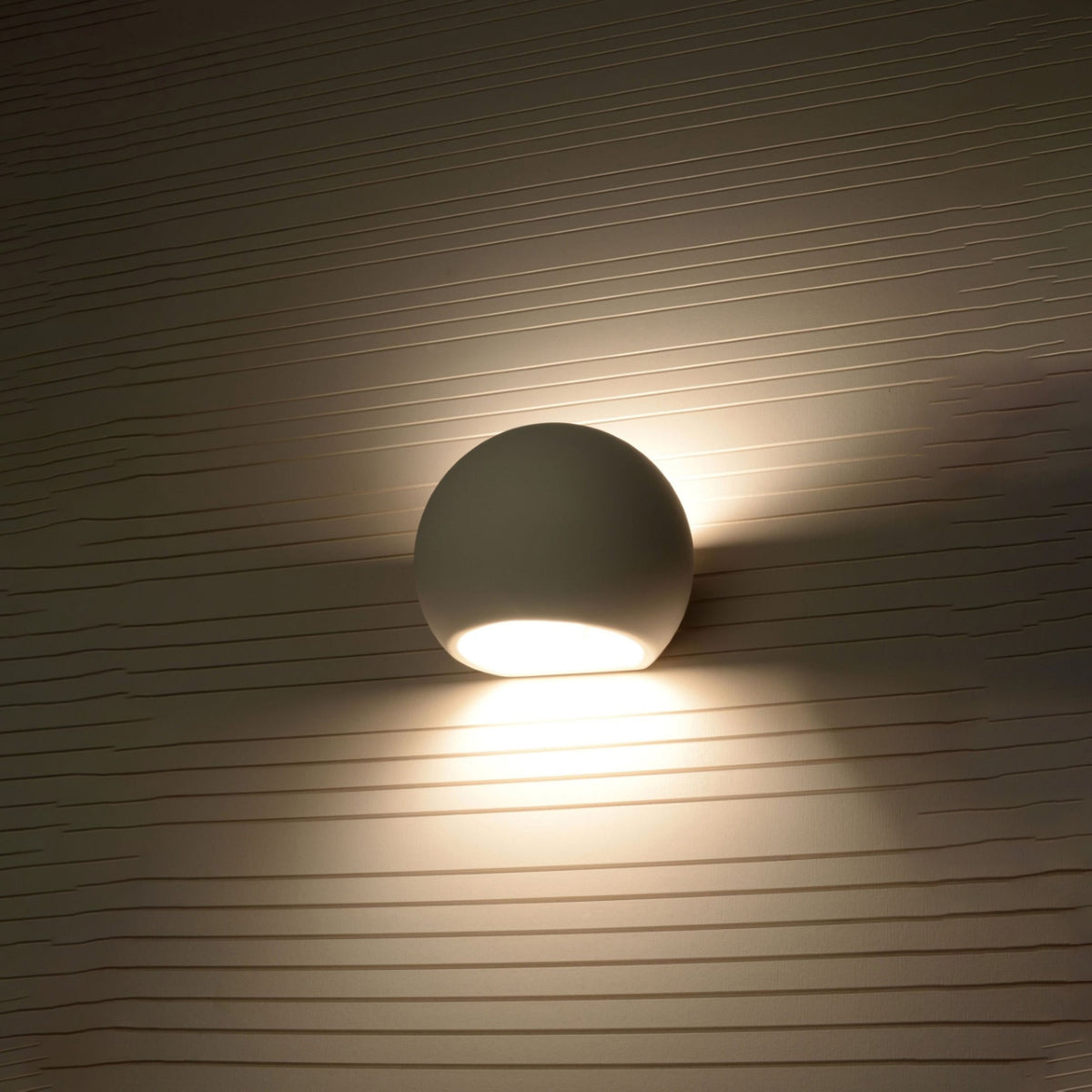 Applique murale Globe blanche allumée sur un mur strié avec deux halos de lumière