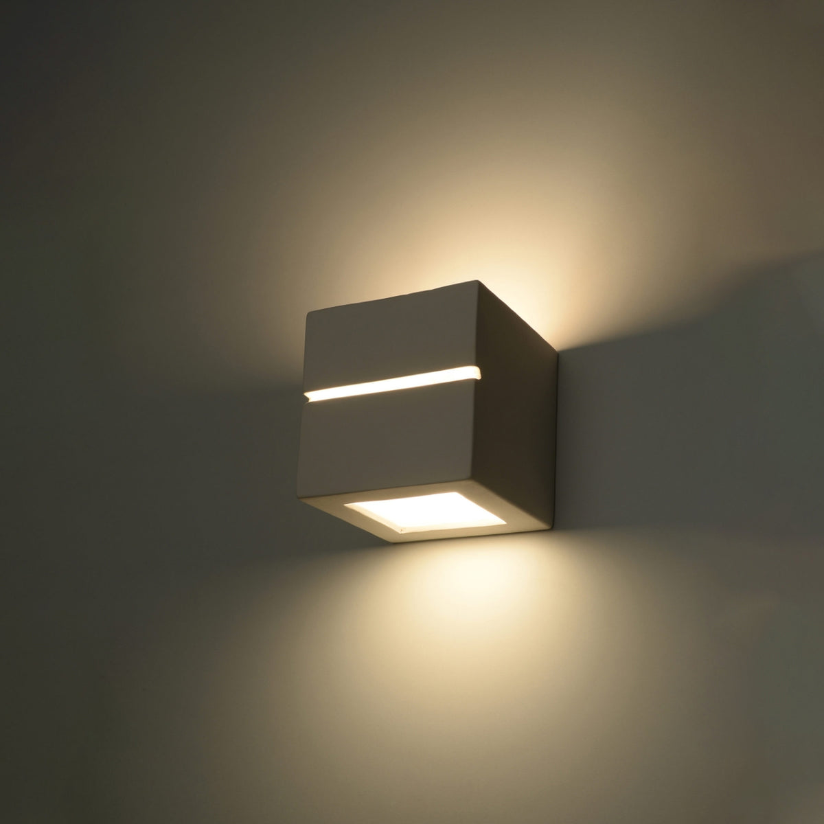 Applique Leo Line allumée sur un mur sombre avec un halo vers le haut et une nappe de lumière vers le bas