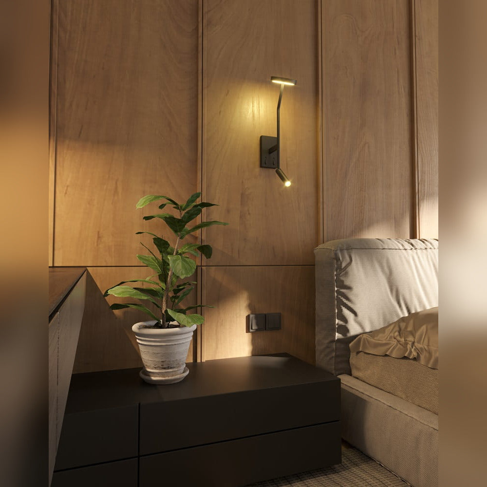 Applique liseuse Ibiza noire allumée sur un mur en bois au-dessus d'une table de chevet près d'un lit