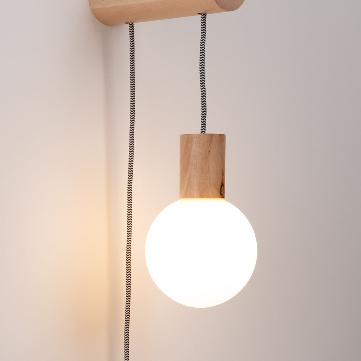 Globe en verre opale allumé sous la douille en hêtre de l'applique Nimbi