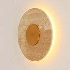 Applique murale Sun allumée vue de trois quarts avec le halo de lumière chaude autour du disque de travertin