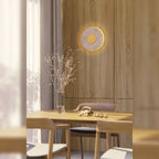 Applique Sun allumée sur un mur en bois clair au-dessus d'une table à manger avec son halo lumineux