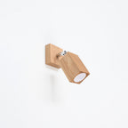 Applique Keke en chêne fixée sur un mur blanc avec sa platine carrée et son articulation métallique