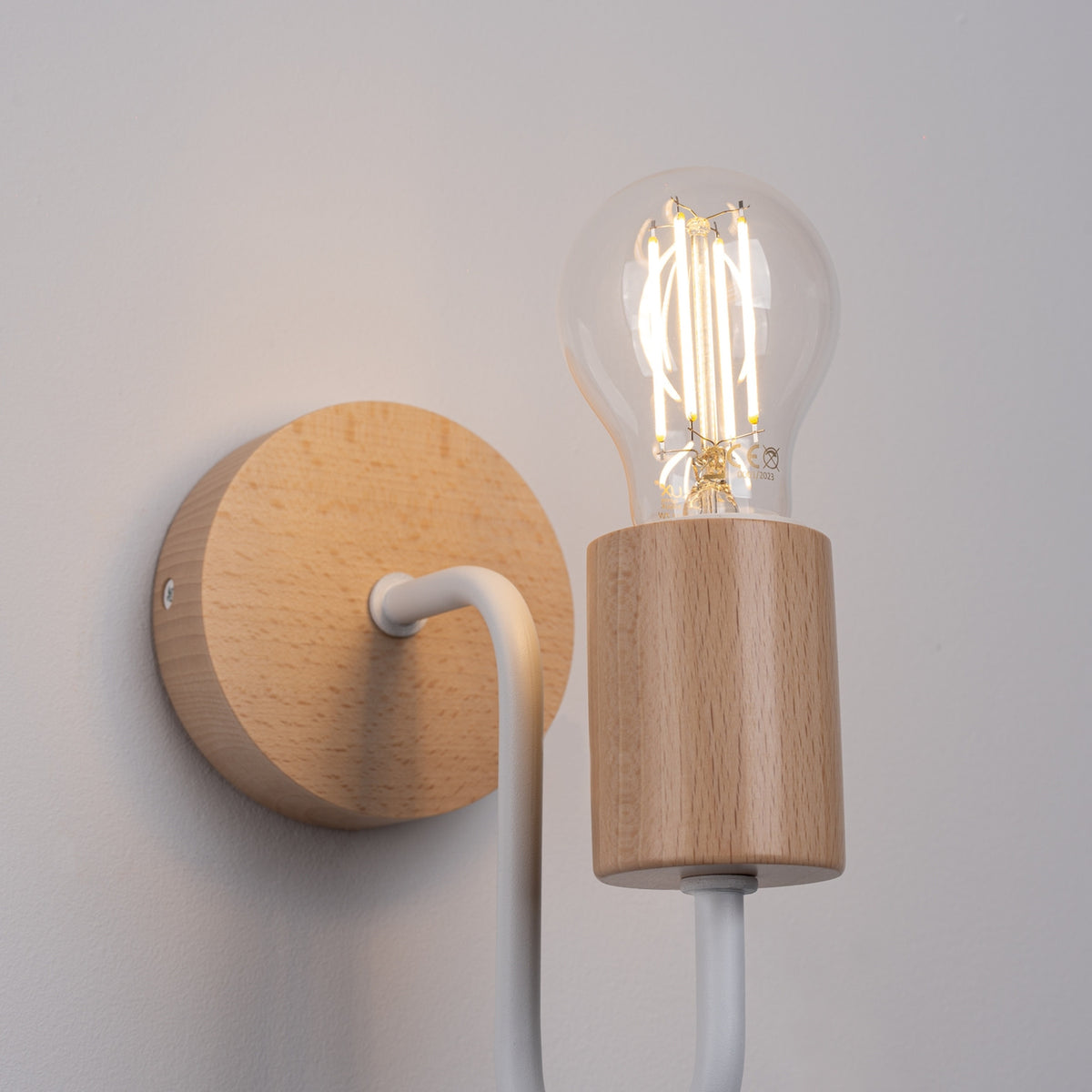 Gros plan de l'applique Timbo métal blanc allumée avec ampoule à filament sur porte-douille en bois