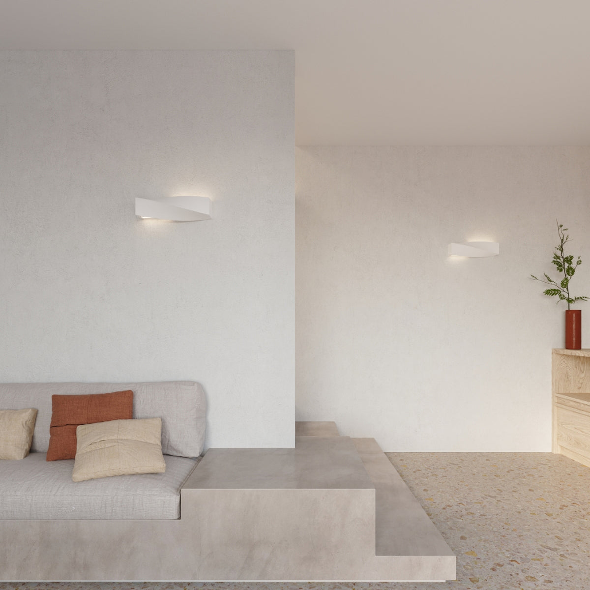 Deux appliques Sigma céramique blanche allumées sur les murs clairs d'un salon avec canapé et sol en terrazzo