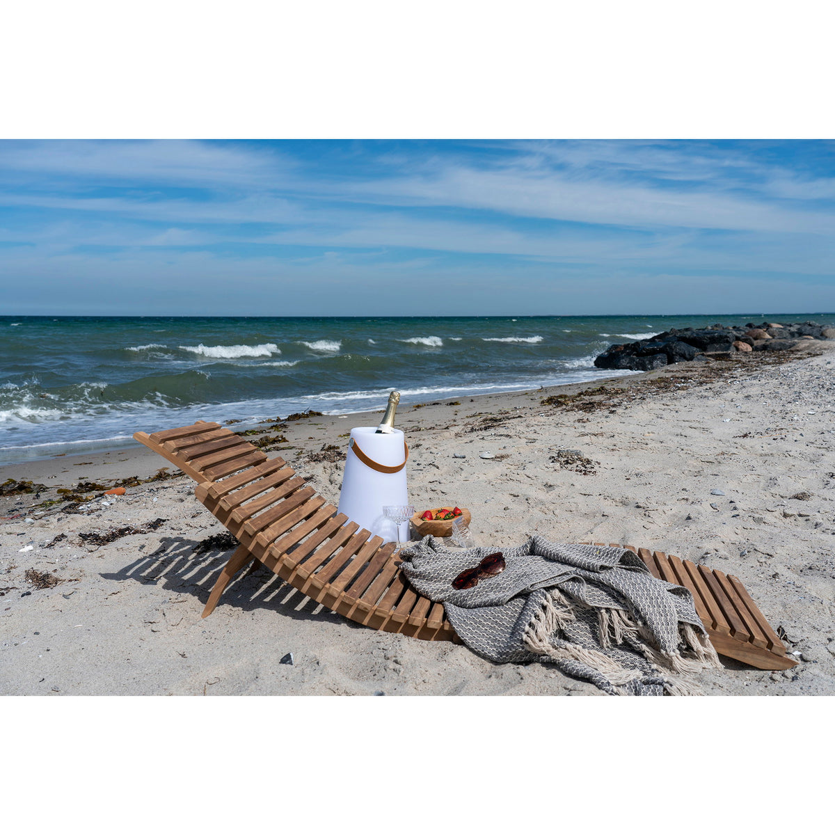 Bain de soleil Arrieta en teck sur le sable avec un plaid gris lunettes de soleil et coupe de fraises