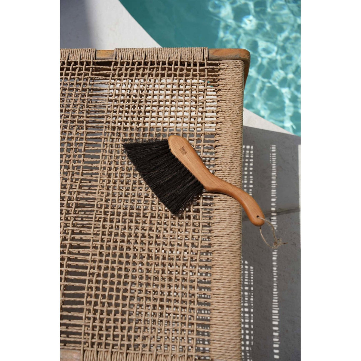 Balayette en teck posée sur une assise tressée au bord d'une piscine