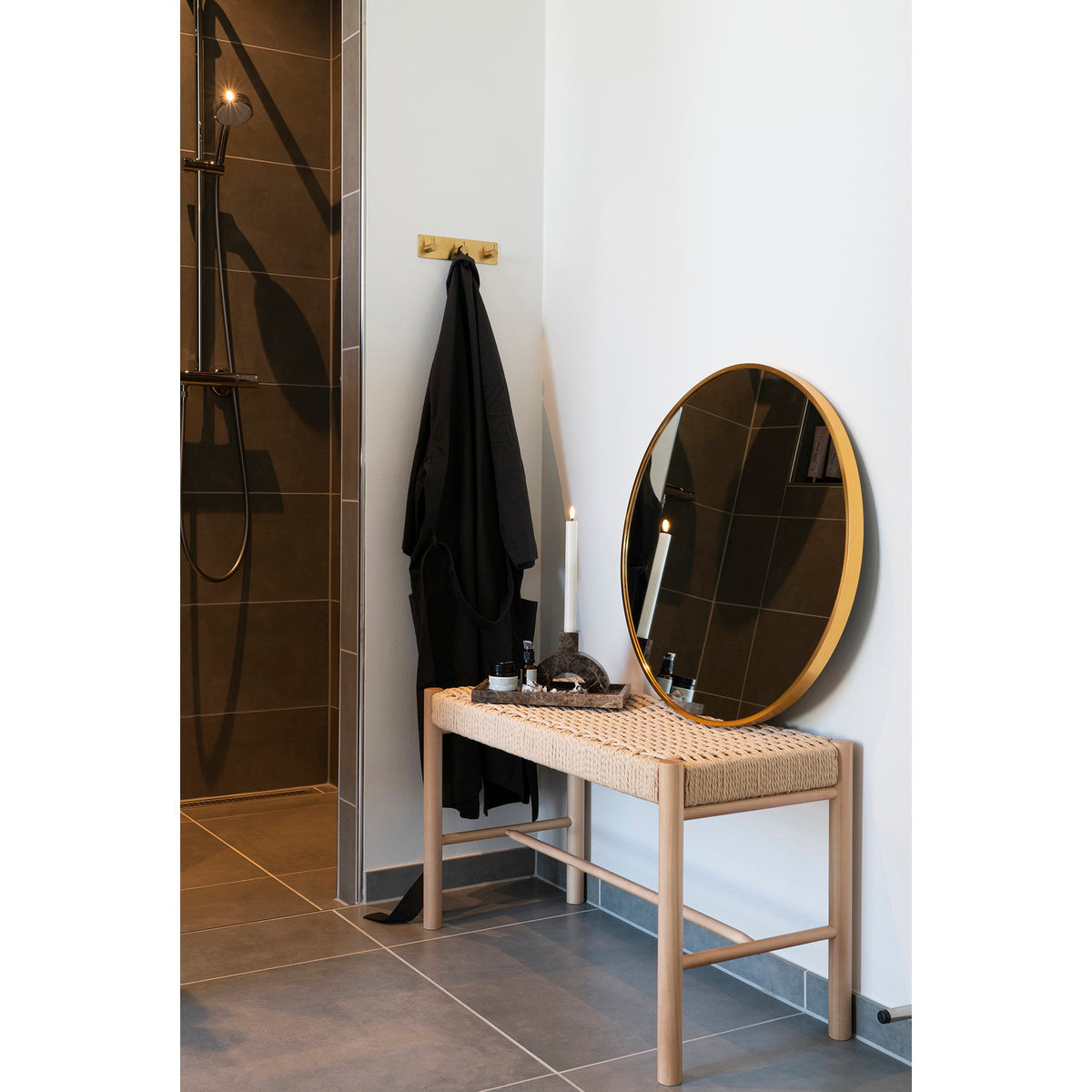 Banc Abano dans une salle de bain portant un miroir rond doré un plateau et une bougie