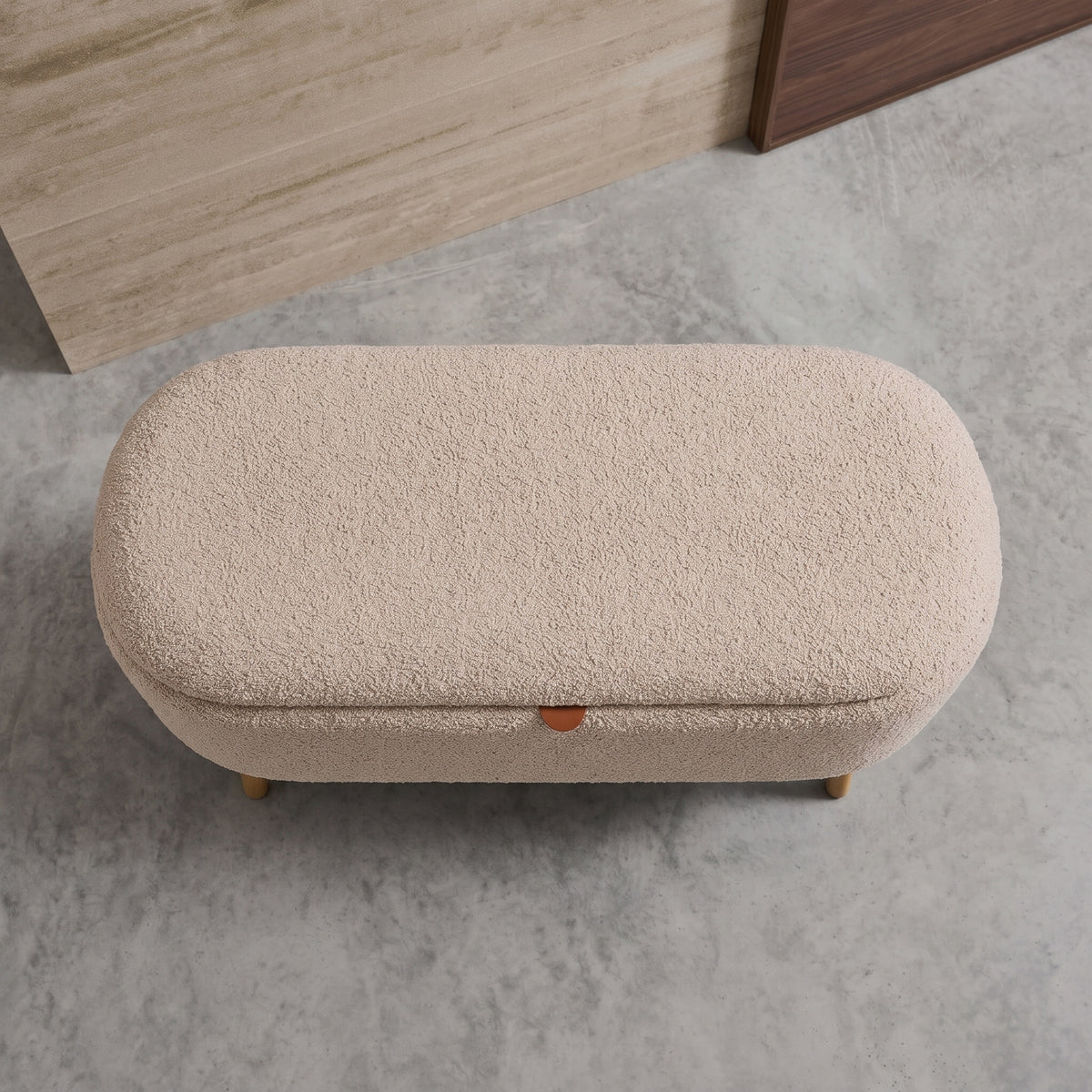 Banc coffre Harlow bouclé taupe vu de dessus, assise bombée et tirette cognac, sur un sol en béton ciré