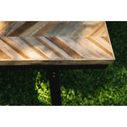 Angle de l'assise en teck à chevrons du banc Herringbone et son cadre en fer noir sur une pelouse