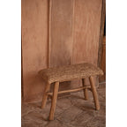 Banc Raffia en raphia et teck de trois quarts devant un mur en enduit terracotta sur un sol en pierre