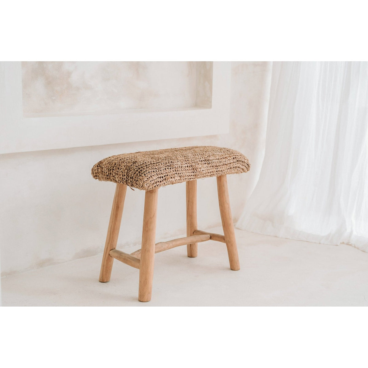 Banc Raffia en raphia et teck dans une pièce blanche près d'un voilage