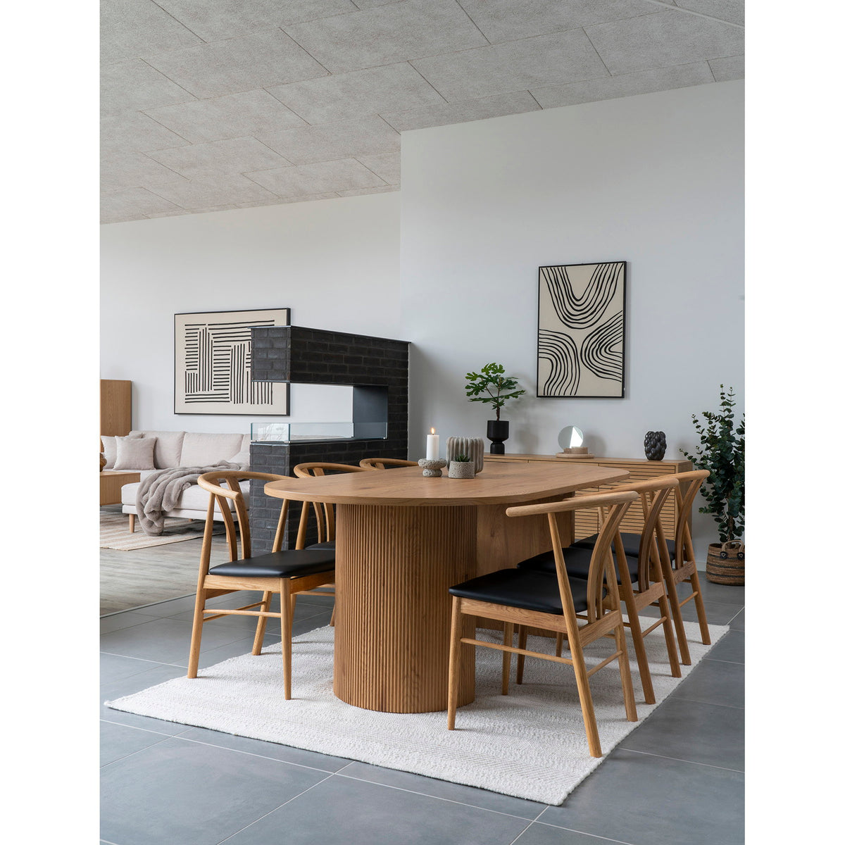 Salle à manger avec une table en bois à pied cannelé et la boîte en travertin naturel posée sur le buffet du fond