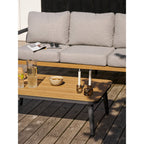Bougeoirs en verre fumé brun avec bougies au bout d'une table basse en bois devant un canapé de terrasse gris