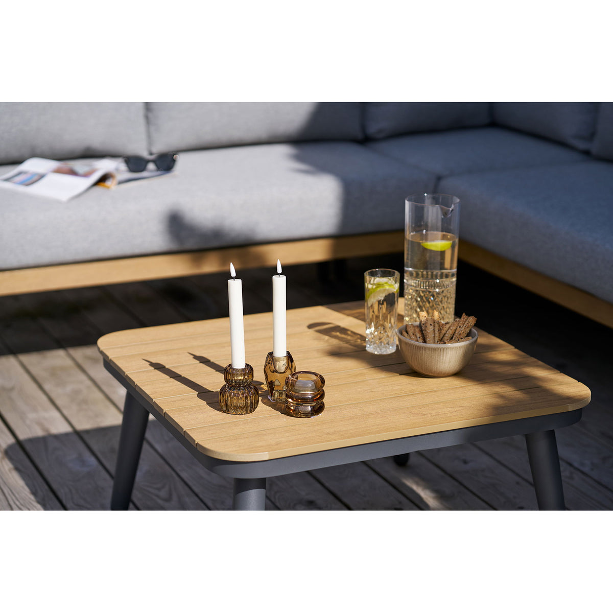 Bougeoirs en verre fumé brun avec deux bougies chandelles et une chauffe-plat sur une table basse de terrasse en bois
