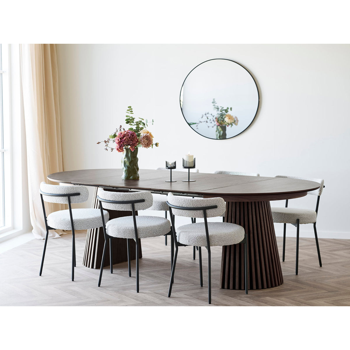 Bouquet artificiel dans un vase vert foncé sur une table ovale en bois foncé devant un miroir rond