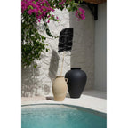 Branche Palmeira noire dans une amphore beige à côté d'une grande jarre noire au bord d'une piscine sous un bougainvillier
