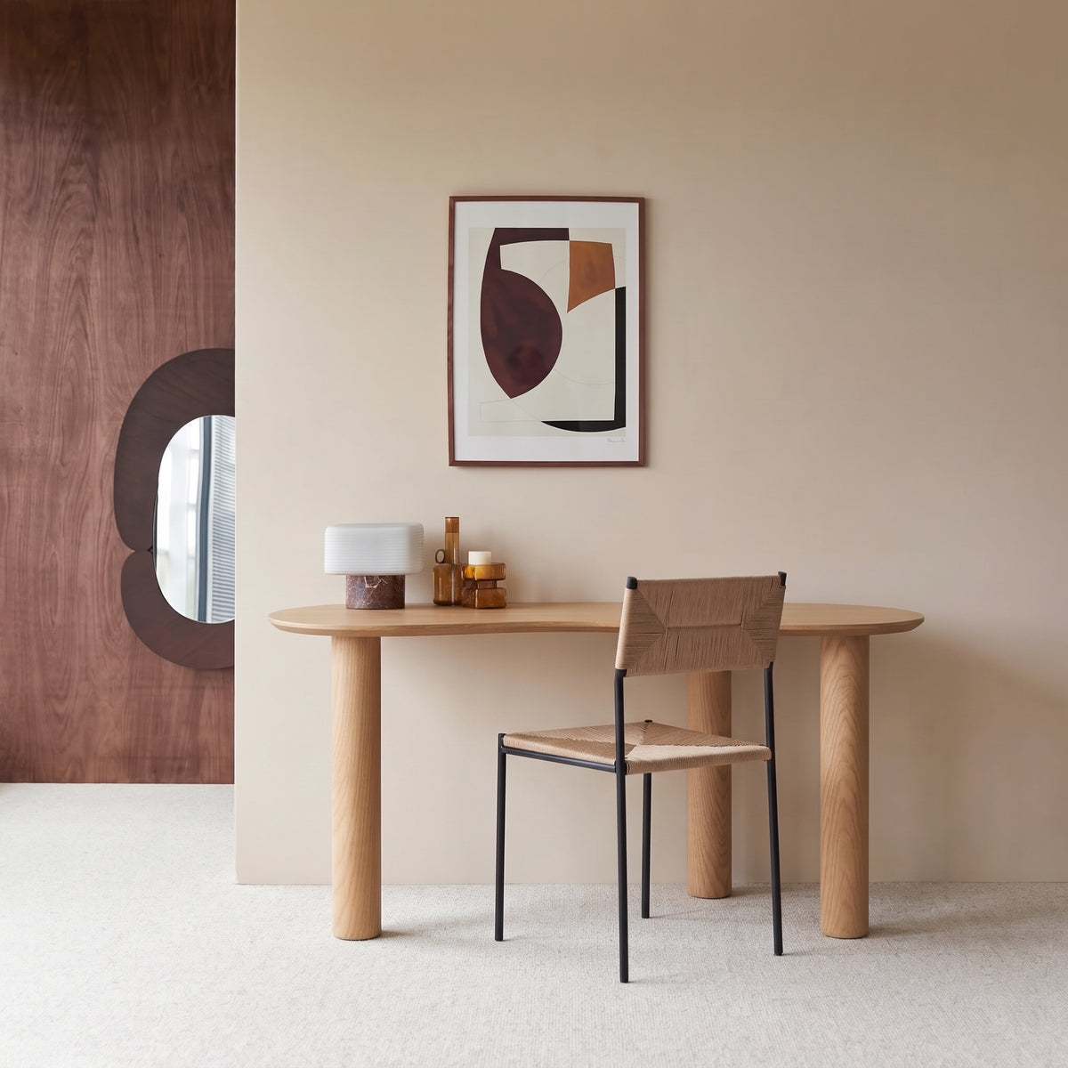 Bureau Livigno devant un mur beige, avec une chaise à assise tressée, un tableau abstrait et une lampe posée sur le plateau