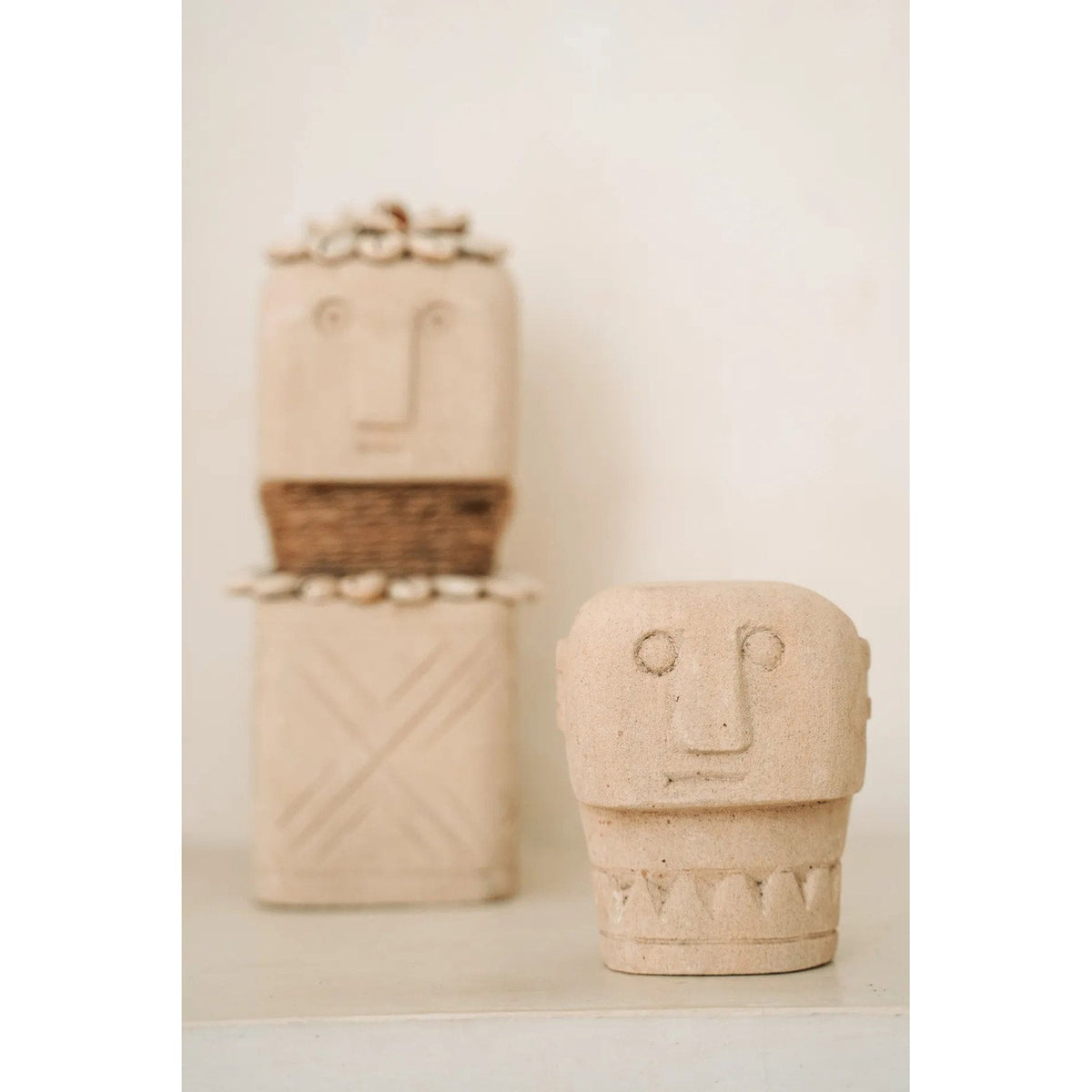Buste Sumba en grès clair au premier plan devant une statuette Sumba ornée de cauris