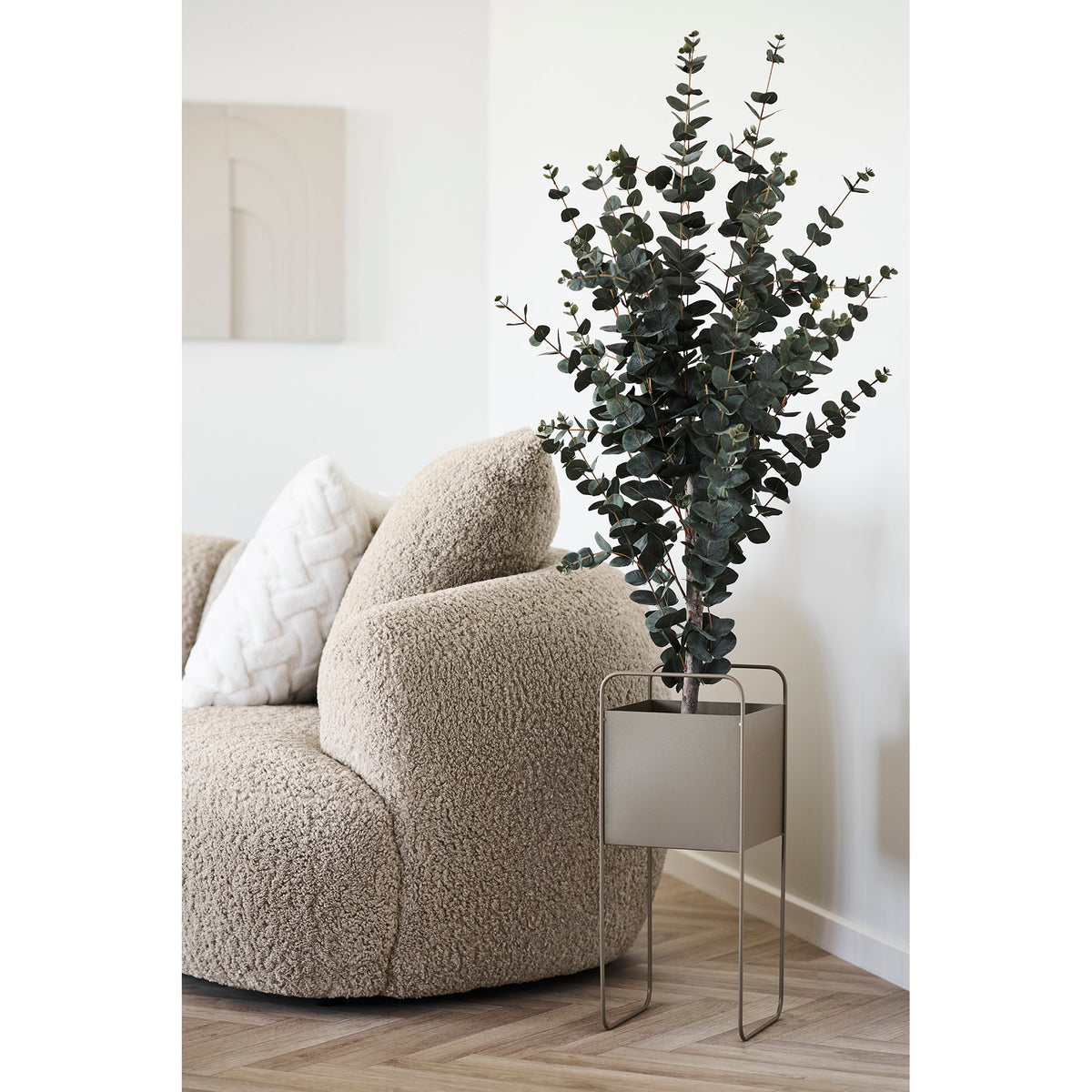 Cache-pot carré en acier taupe garni d'un eucalyptus à côté d'un canapé en bouclette