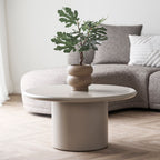 Cache-pot marron avec une plante verte posé sur une table basse ronde beige devant un canapé en bouclé gris