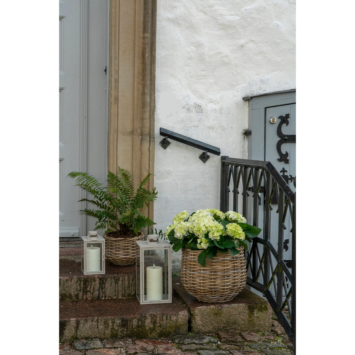 Cache-pots Pulo en rotin kubu avec une fougère et un hortensia blanc sur les marches d'une entrée près de deux lanternes