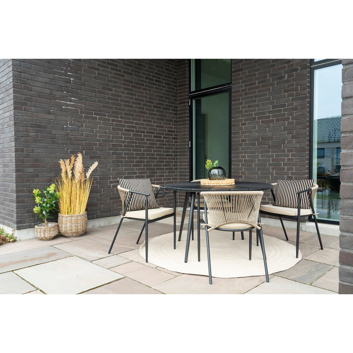 Cache-pots Pulo en rotin kubu garnis de plantes sur une terrasse près d'une table ronde noire et de fauteuils en corde