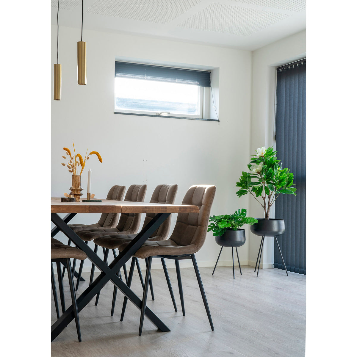 Salle à manger avec table en bois et chaises taupe et deux cache-pots Ardola noirs garnis de plantes près de la baie