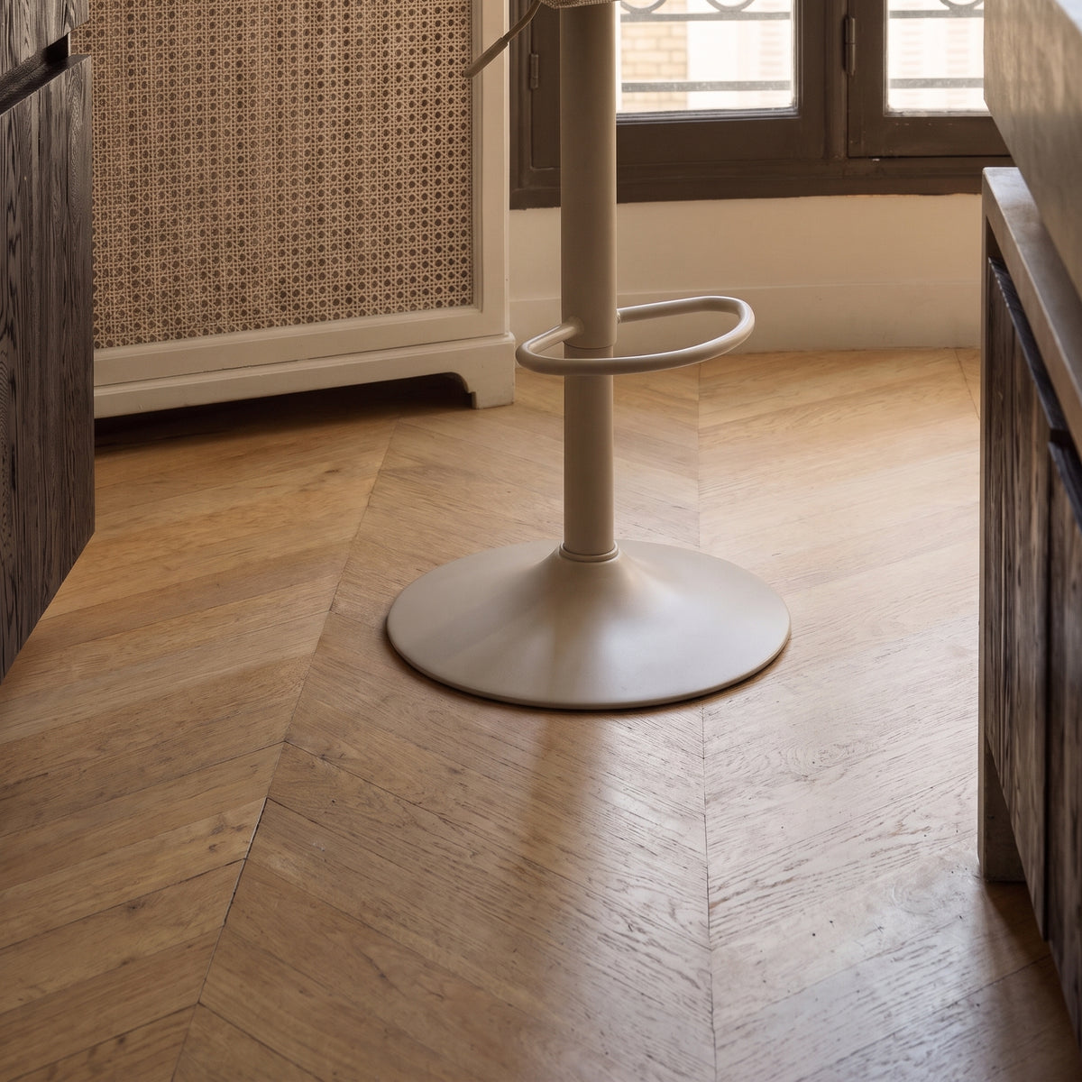 Pied trompette et repose-pieds de la chaise de bar Middelfart, sur un parquet en chevrons, au pied d'un plan de travail