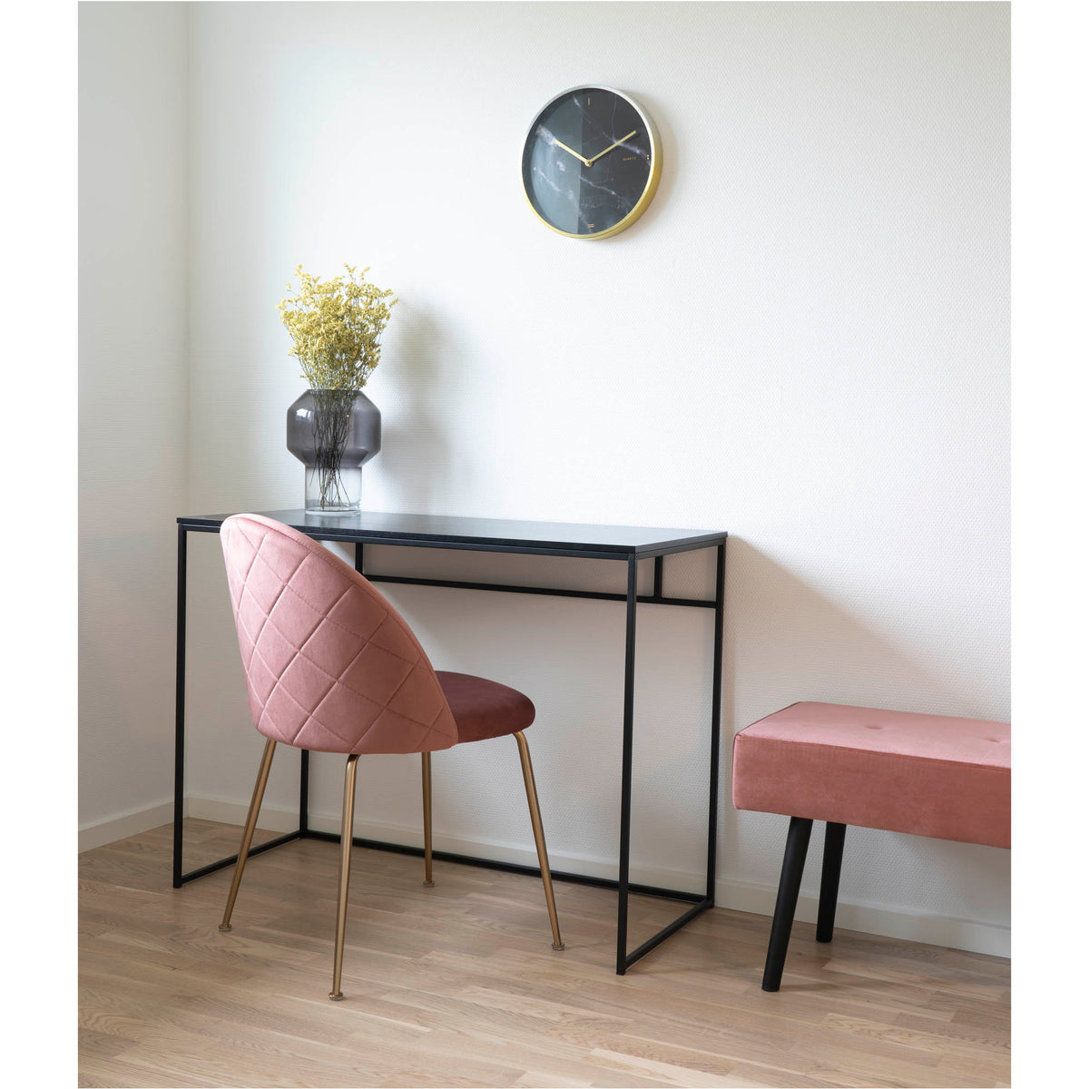 Chaise Geneve velours rose devant un bureau fin en métal noir sous une horloge murale