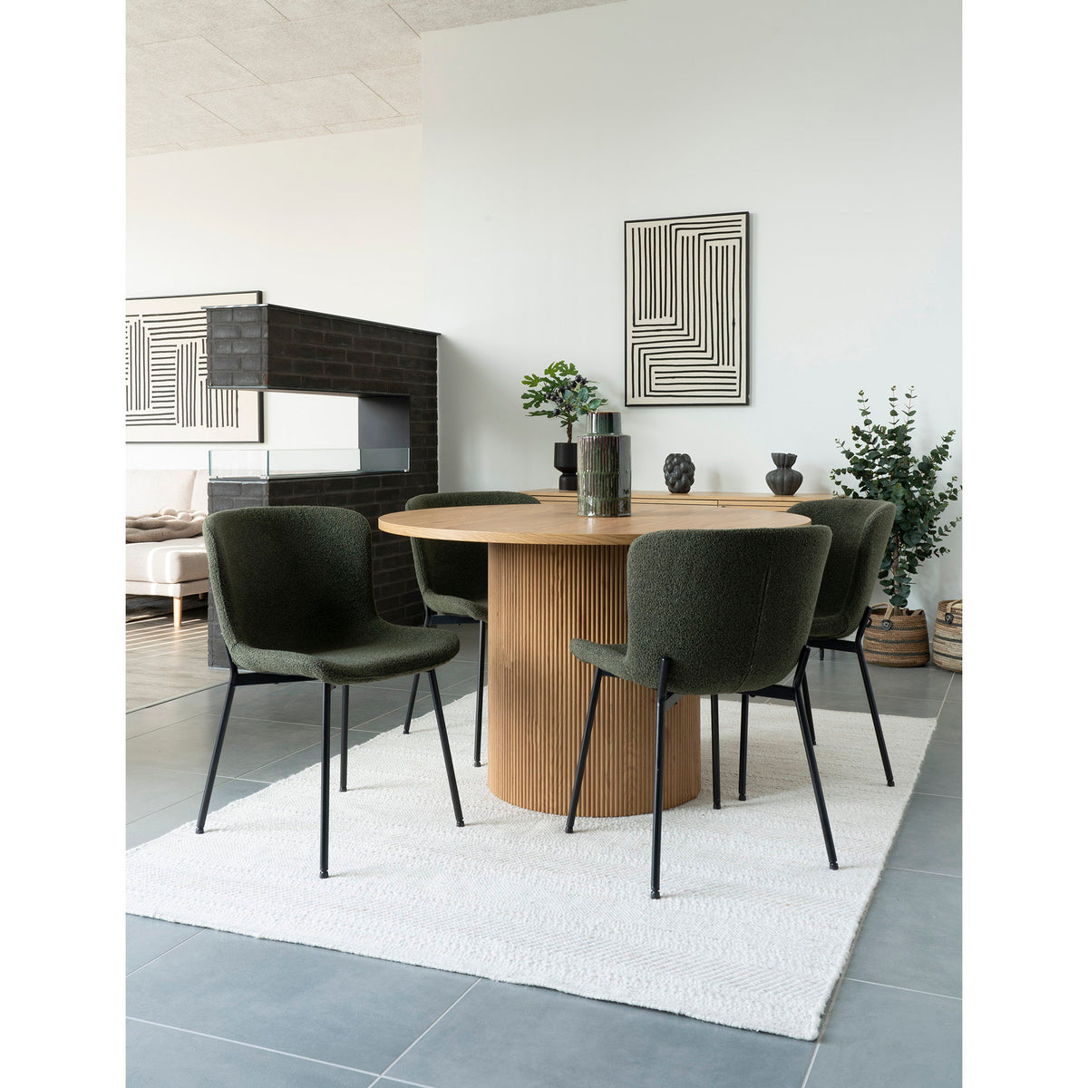 Quatre chaises Maceda bouclé vert foncé autour d'une table ronde en bois à pied cannelé sur un tapis clair