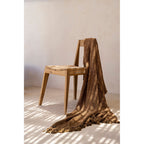 Chaise Paxi en teck naturel avec un plaid brun tissé drapé sur le dossier devant un mur clair