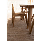 Chaise Paxi en teck vue de profil près d'une table en bois sur un tapis tressé