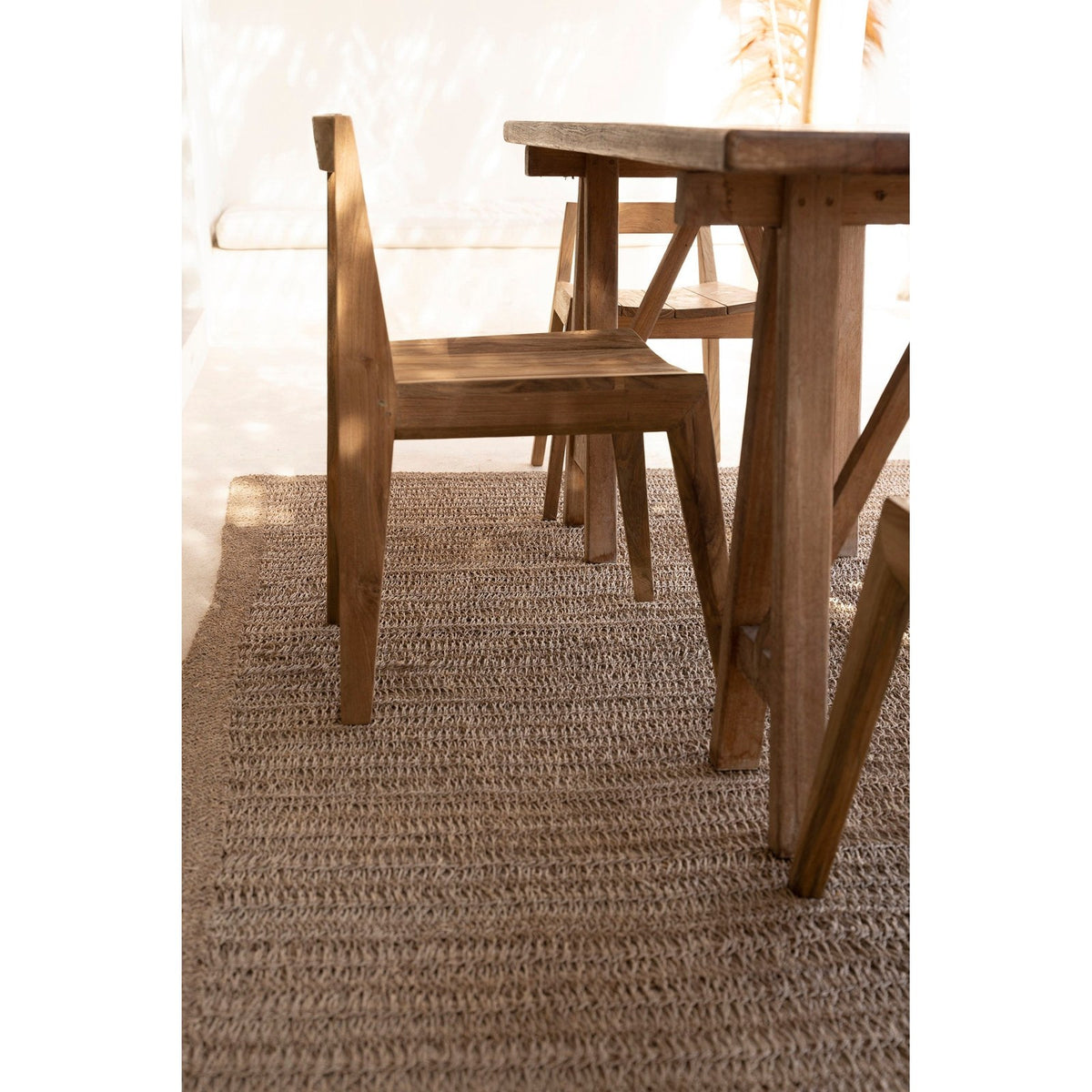 Chaise Paxi en teck vue de profil près d'une table en bois sur un tapis tressé