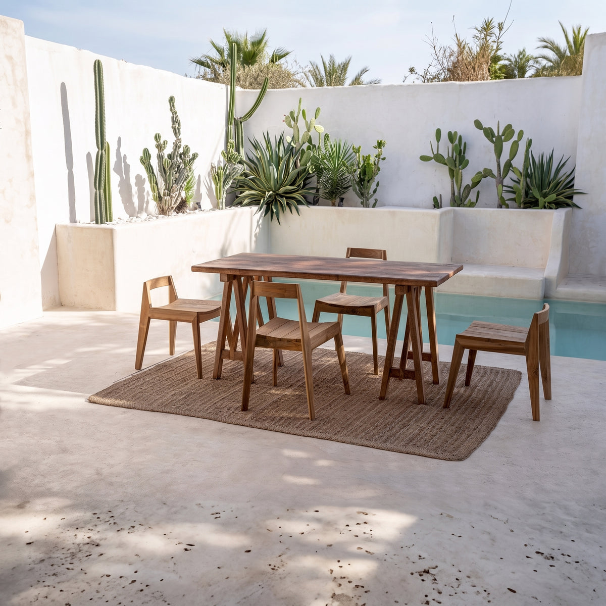 Quatre chaises Paxi en teck naturel autour d'une table, dans un patio planté de cactus près d'une piscine