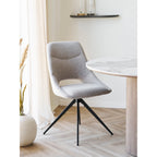 Chaise pivotante Dokka près d'une table ronde à plateau veiné blanc et pied cannelé devant une fenêtre
